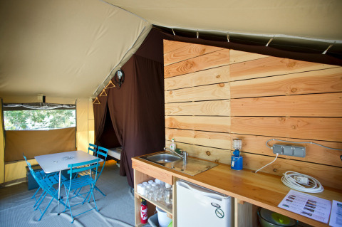 Intérieur d'une tente Safari Toile&Bois Sweet à Huttopia le Moulin, avec coin repas et kitchenette.