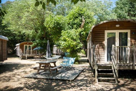 Outdoor view of Gypsy caravan cabins and picnic area at Huttopia le Moulin, France, surrounded by trees.