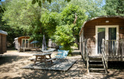 Außenaufnahme von Gypsy Caravan Hütten und Picknickbereich im Huttopia le Moulin, Frankreich, umgeben von Bäumen.