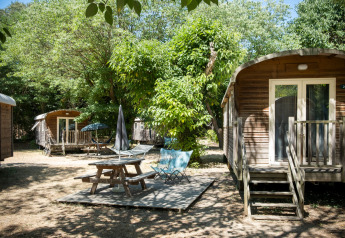 Vista esterna delle cabine Gypsy caravan e area picnic a Huttopia le Moulin, Francia, circondato da alberi.