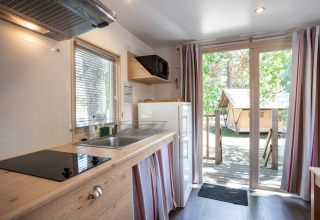 Cocina luminosa en una caravana gitana en Huttopia le Moulin, Francia, con vista a la terraza y carpa exterior.