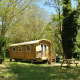 Gypsy caravan-træhytte placeret i en frodig grøn skov med picnicbord foran og bil i baggrunden.