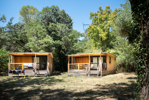 Twee houten chalets van Chalet Evasion staan tussen bomen en natuur op een zonnige dag.