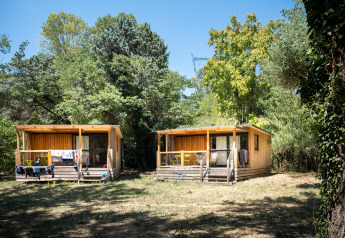 To trækabiner ved Chalet Evasion omgivet af grønt løv og skygge på en solrig dag i naturen.