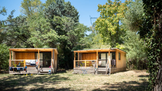 Due chalet in legno del Chalet Evasion circondati dal verde e dagli alberi in una giornata di sole.
