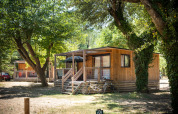 Houten chalet met terras en fietsen ervoor, gelegen tussen bomen bij Huttopia le Moulin, Frankrijk.