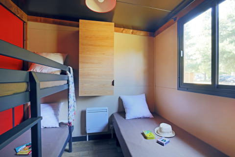 Luminoso cuarto de cabaña con litera, cama individual, amplia ventana y decoración sencilla y acogedora.
