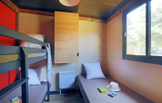 Helles Kabinenzimmer mit Etagenbett, Einzelbett, großem Fenster, einfacher Einrichtung und Holzboden.