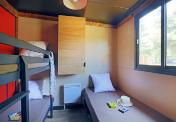 Luminoso cuarto de cabaña con litera, cama individual, amplia ventana y decoración sencilla y acogedora.