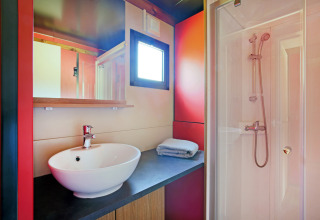 Baño moderno de cabaña con lavabo redondo, espejo, ventana, toallas dobladas y cabina de ducha.