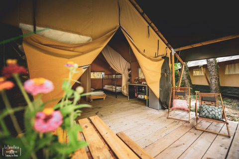 Tenda safari Saadani a Huttopia Vallée du Lot in Francia con terrazza in legno, sedie e fiori in primo piano.