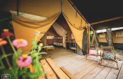 Tenda safari Saadani a Huttopia Vallée du Lot in Francia con terrazza in legno, sedie e fiori in primo piano.