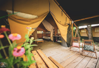 Tente safari Saadani à Huttopia Vallée du Lot, France, avec terrasse en bois, chaises et fleurs au premier plan.