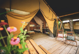 Safari-Zelt Saadani im Huttopia Vallée du Lot in Frankreich mit Holzterrasse, Stühlen und Blumen im Vordergrund.
