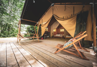 Tienda safari Tent Saadani en Huttopia Vallée du Lot en Francia, con plataforma de madera y muebles afuera.
