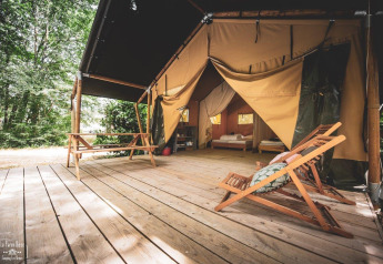 Tienda safari Tent Saadani en Huttopia Vallée du Lot en Francia, con plataforma de madera y muebles afuera.