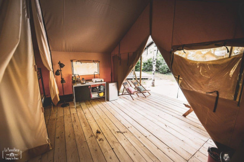 Intérieur d'une tente safari spacieuse avec plancher en bois, kitchenette et fauteuils sur la terrasse.