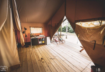 Ruim safaritent interieur met houten vloer, keukenblok, ligstoelen en open tentflappen in Frankrijk.