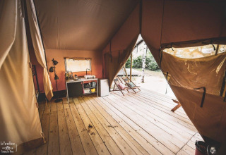 Interior of a spacious safari tent with wooden floor, kitchenette, lounge chairs, and open tent flaps.