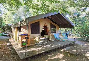 Safari Sweet Tent con veranda in legno e arredi da esterno, circondata da alberi e auto parcheggiate.