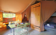 Innenraum eines Sweet Tent Safari-Zelts bei Huttopia Vallée du Lot, Frankreich, mit Tisch und Betten.