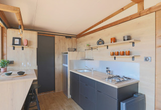 Cocina de tienda safari moderna con detalles de madera, estantes abiertos y comedor en Huttopia Vallée du Lot, Francia.