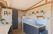 Cocina de tienda safari moderna con detalles de madera, estantes abiertos y comedor en Huttopia Vallée du Lot, Francia.