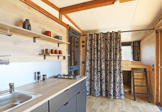 Interior de una tienda safari Arizona en Huttopia Vallée du Lot, Francia, con cocina moderna y litera.