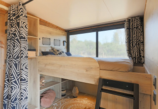 Interior de una tienda safari estilo Arizona en Huttopia Vallée du Lot, con cama alta, ventana y cortinas.