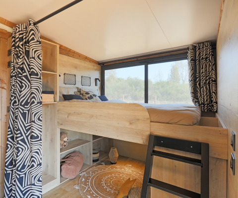 Interior de una tienda safari estilo Arizona en Huttopia Vallée du Lot, con cama alta, ventana y cortinas.