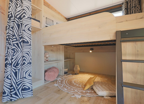 Cozy bunk bed nook with patterned curtains and reading area inside a safari tent at Huttopia Vallée du Lot, France.