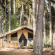 Safari telt Toile&Bois Sweet midt i en fyrreskov, udstyret med terrasse, borde og stole til camping.