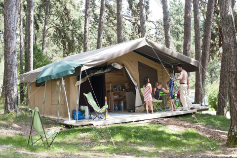 Famiglia che si rilassa davanti a una tenda safari nei boschi di Huttopia Divonne Les Bains, Francia.