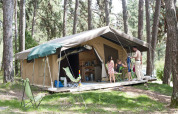 Family relaxing at a safari tent campsite in the woods at Huttopia Divonne Les Bains, France.