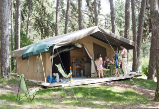 Familie entspannt vor einem Safari-Zelt im Wald im Huttopia Divonne Les Bains, Frankreich.