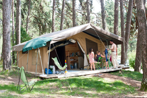 Famiglia si rilassa davanti alla tenda safari Sweet di Huttopia Divonne Les Bains, immersa nei boschi francesi.