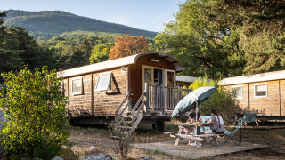 Two people by a picnic table outside the Gypsy caravan cabin in a scenic, wooded mountain area.