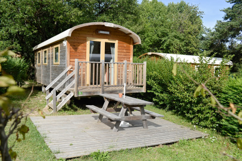 Caravana gitana en Huttopia Divonne Les Bains, Francia, con terraza de madera y mesa de picnic exterior.