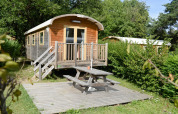 Caravana gitana en Huttopia Divonne Les Bains, Francia, con terraza de madera y mesa de picnic exterior.
