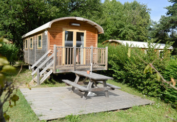 Roulotte à Huttopia Divonne Les Bains en France, avec terrasse en bois et table de pique-nique devant.