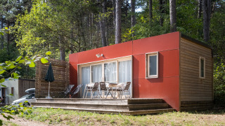 Casa móvil Vancouver: Moderna cabaña de madera con detalles rojos y terraza, situada en un bosque.
