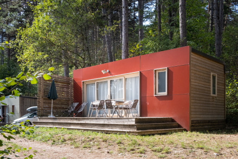 Mobilhjem Vancouver: En moderne træhytte med terrasse, omgivet af skov og havestole foran.