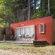 Casa móvil Vancouver: Moderna cabaña de madera con detalles rojos y terraza, situada en un bosque.