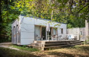 Mobile home Vancouver cabin at Huttopia Divonne Les Bains in France, surrounded by trees and wooden deck.