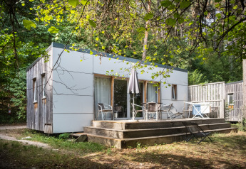 Mobile home Vancouver cabin at Huttopia Divonne Les Bains in France, surrounded by trees and wooden deck.
