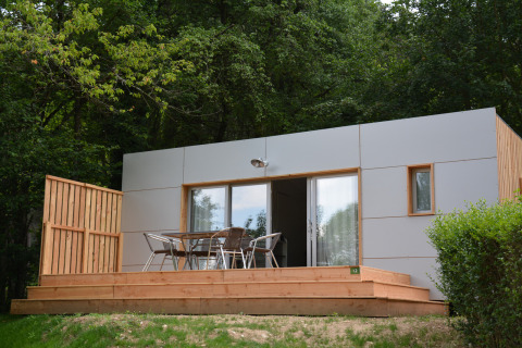 Casa móvil Vancouver moderna en Huttopia Divonne Les Bains, Francia, con terraza de madera y sillas de exterior.