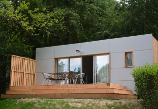 Casa móvil Vancouver moderna en Huttopia Divonne Les Bains, Francia, con terraza de madera y sillas de exterior.