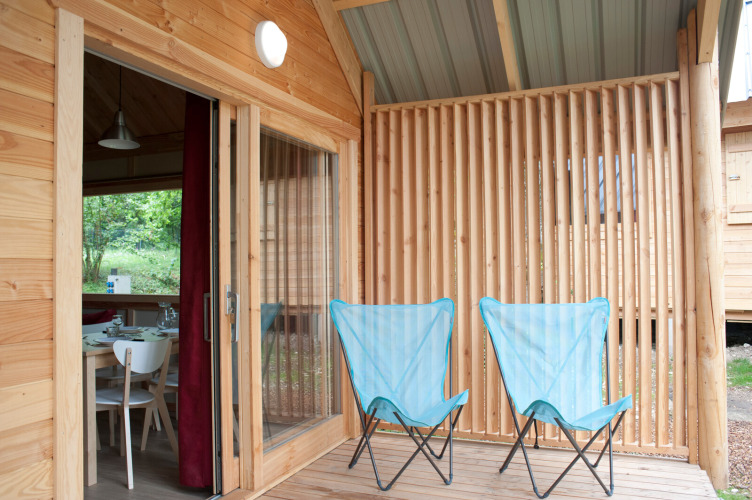 Wooden patio with two blue camping chairs at Chalet Montana, Huttopia Divonne Les Bains in France.