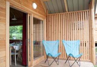 Holzterrasse mit zwei blauen Campingstühlen am Chalet Montana, Huttopia Divonne Les Bains, Frankreich.