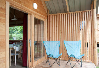 Terraza de madera con dos sillas de camping azules en Chalet Montana, Huttopia Divonne Les Bains, Francia.